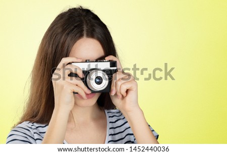 Portrait of a young smiling woman filming with retro camera isolated