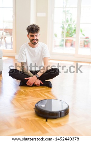 Young man using automatic vacuum cleaner to clean the floor, controling machine housework robot