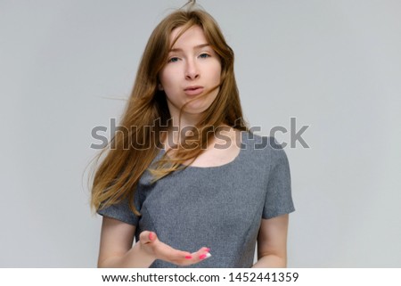 Portrait below the chest of a young pretty brunette girl woman with beautiful long hair on a white background in a gray dress. He talks, smiles, shows his hands with emotions in various poses.
