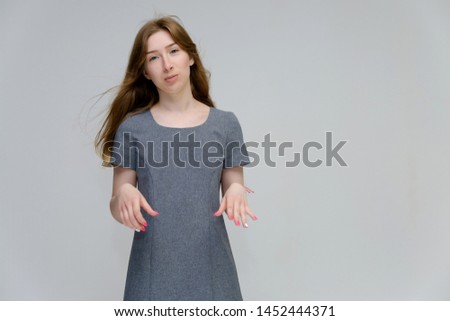 A portrait below belt of a young pretty brunette girl woman with beautiful long hair on a white background in a gray dress. He talks, smiles, shows his hands with emotions in various poses.