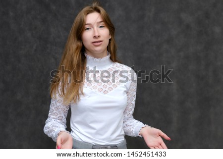 Portrait to the waist of a young pretty brunette girl woman with beautiful long hair on a gray background in a white jacket. He talks, smiles, shows his hands with emotions in various poses.