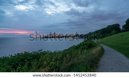 Long Winding Path Along Lake Erie At Edgewater Park With Downtown Cleveland's Skyline In The Distant Background With Overhead Clouds And A Little Sunrise Color.
