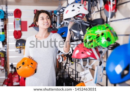 Young woman choosing new helmet in sports equipment store