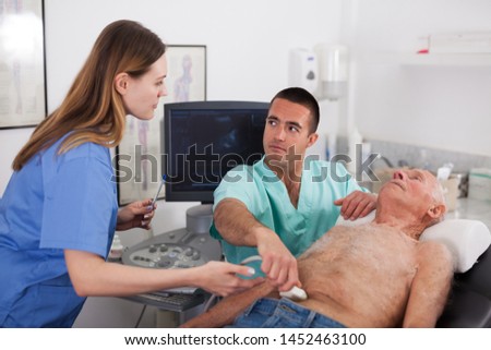 Young woman and man doctors examination elderly man at abdomen with ultrasonography device