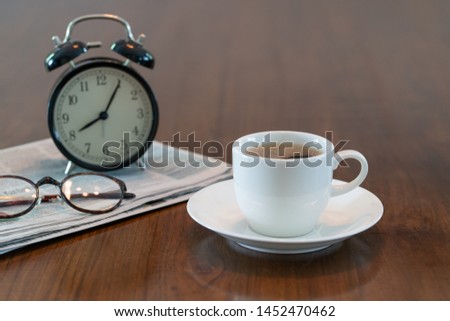 Hot coffee cup and vintage clock newspaper reading glasses on brown wood table