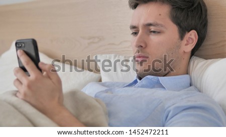 Young Man Using Smartphone in Bed