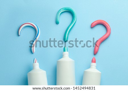 Question mark from toothpaste. Concept of choosing good toothpaste for teeth whitening. Tube of colored toothpaste on blue background. Copy space for text Royalty-Free Stock Photo #1452494831