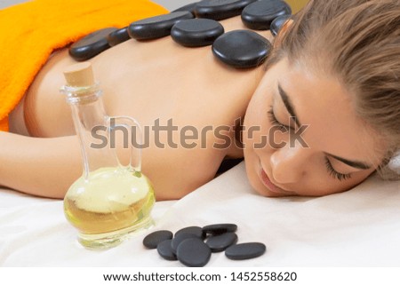 Spa hot stone massage. Professional beautician massaging female back by stones. Relaxed girl enjoying body treatment at wellness center