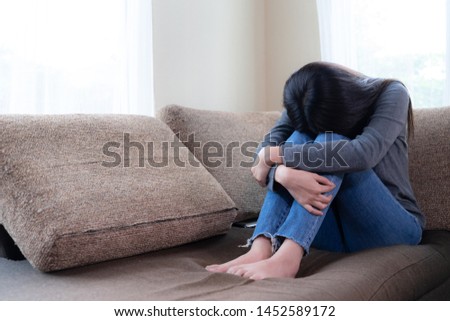 Unhappy asian pretty young woman siting alone on couch with feeling sadness