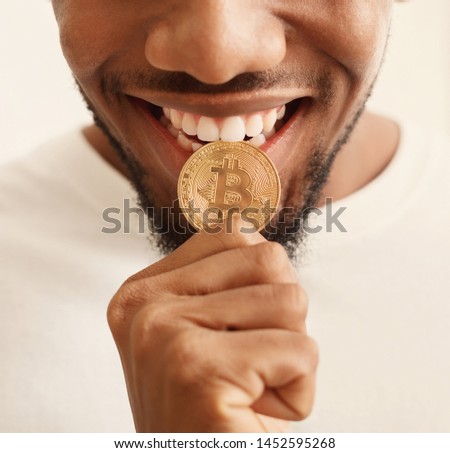Cryptocurrency. African-american man biting golden bitcoin, close up portrait Royalty-Free Stock Photo #1452595268