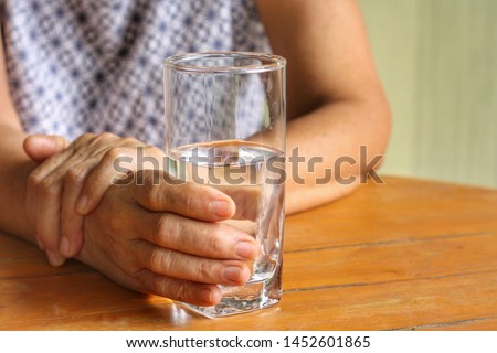 Elderly woman is holding his hand while drinking water because Parkinson's disease.Tremor is most symptom and make a trouble for doing activities such as eat or drink.Health care or elderly concept. Royalty-Free Stock Photo #1452601865