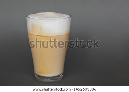 A large transparent glass filled with Latte cooked in a third wave coffee shop is photographed on a gray, isolated background, photo for the menu