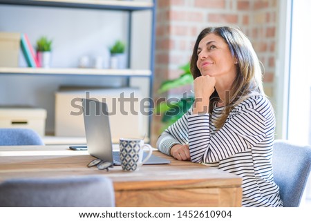 Middle age senior woman sitting at the table at home working using computer laptop serious face thinking about question, very confused idea