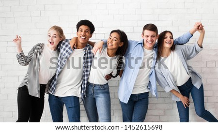 Diverse teens embracing and posing over white brick wall, looking at camera Royalty-Free Stock Photo #1452615698