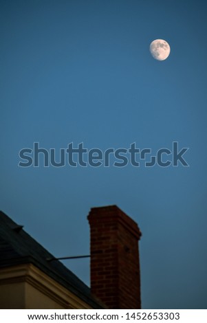 Chimney and roof unfocused, with the moon in the background. Concept of home and night.