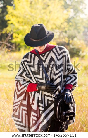Beautiful woman in poncho, hat and gloves is walking across the meadow