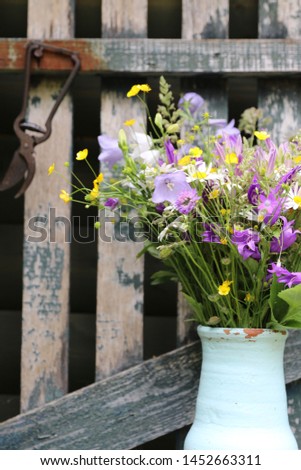 Bouquet of wild flowers in vintage ceramic jar on weathered wooden fence background, rustic style, outdoor and space