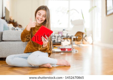 Beautiful young girl kid using digital touchpad tablet sitting on the floor happy with big smile doing ok sign, thumb up with fingers, excellent sign