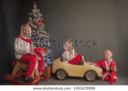 Happy children are dressed in festive costume of Santa Claus and snowman, carrying decorated Christmas tree with balls and garlands on yellow car, accompanied by rocking horse. Christmas Eve