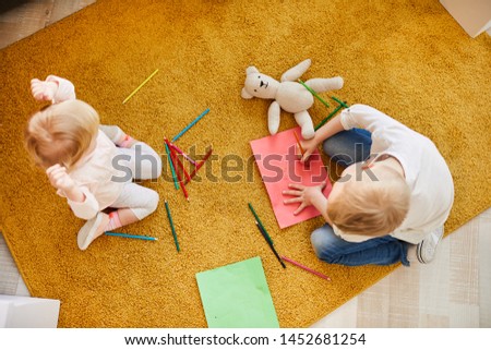 High angle view of curious kids of different ages sitting on comfortable carpet and drawing with colorful pencils on paper