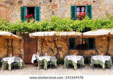 Cafe tables and chairs outside a quaint stone building in Tuscany, Italy Royalty-Free Stock Photo #145269478