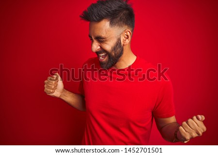 Young handsome indian man wearing t-shirt over isolated red background very happy and excited doing winner gesture with arms raised, smiling and screaming for success. Celebration concept.