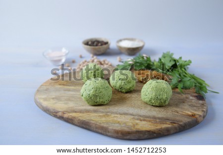 Fresh raw falafel balls of chickpeas, herbs and spices on a wooden cutting board on a light wooden background with ingredients for the preparation. Vegan tacos. Vegetarian healthy food.