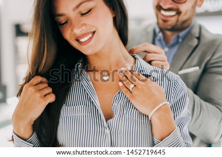 Middle age couple enjoying in shopping at modern jewelry store. Young woman try it out gorgeous necklace and earrings. Royalty-Free Stock Photo #1452719645