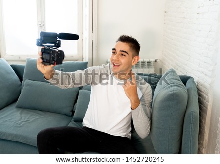 Young cute man in casual clothes style holding camera shooting self portrait photo or recording video in streaming at home. In Social Media Influencer, internet followers and blogger concept.