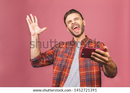 Portrait of an excited young man looking at mobile phone isolated over pink background, winner, celebrating.