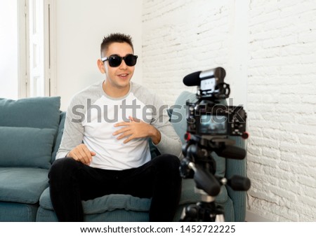 Happy trendy caucasian male on his twenties filming video blog on camera with tripod for online followers at home. In social media, Influencer, new technology, communication and internet concept.