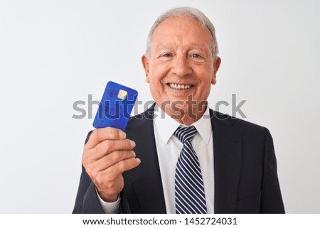 Senior grey-haired businessman holding credit card over isolated white background with a happy face standing and smiling with a confident smile showing teeth
