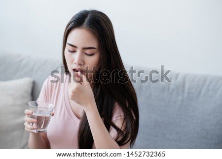Sick woman eating pills with a glass of water in hand.
 Royalty-Free Stock Photo #1452732365