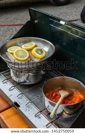 A low FOOD Map dinner of halibut with lemon slices and stewed tomatoes and red peppers cooks on a camp stove on a camping trip.