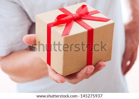 Male hand holding gift box with red ribbon.