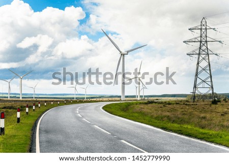 Bend along a country road running through a wind farm. A high voltage electricity pylon is visible on the right side of the picture.