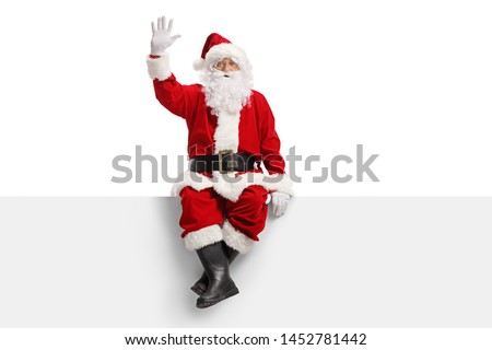 Full length portrait of santa claus sitting on a panel and waving isolated on white background