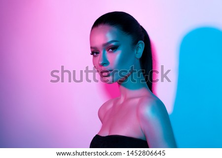 High fashion model woman's face in colorful bright neon UV blue and purple lights. Beautiful girl posing in the Studio, glowing makeup, colorful makeup. Glitter bright neon makeup.  Royalty-Free Stock Photo #1452806645