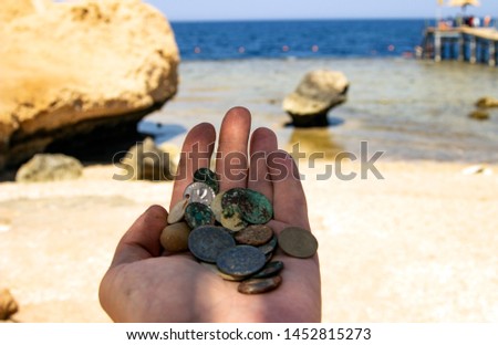 The photo of gold and silver  coins on the hand at the beach backdrop. Treasure searching and tourist adventure background. 