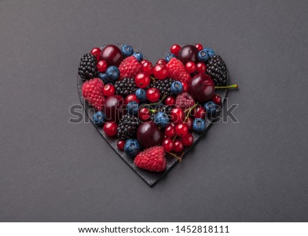Berries overhead fresh heart shaped vibrant arrangement on black background strawberries, blackberries, red currant, cherries and raspberries shiny fruit studio shot