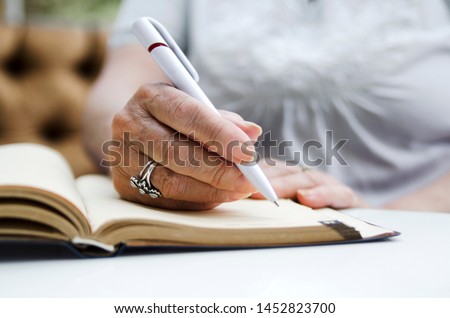 Senior woman writing in note book.Old female hands on paper note writing down a memo for the day  Royalty-Free Stock Photo #1452823700
