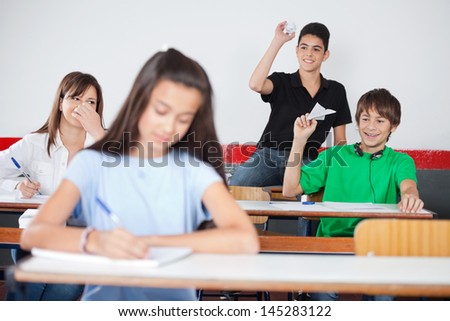 Playful schoolboys throwing paperplane and paperball on girl in classroom Royalty-Free Stock Photo #145283122