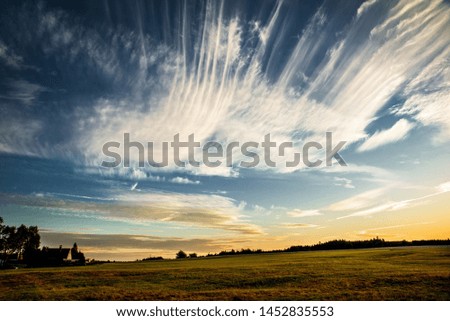 Sky with many nice line clouds "cirrus" at sunset above fields and meadows and small cottage. Czech republic countryside in South Bohemia.