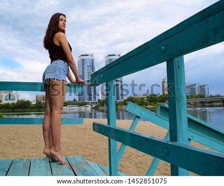 Rear view of the girl in denim shorts on the beach near the city

