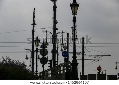 Jumble of Victorian style street gas lamps, modern road signs and overhead wires and tram cables set against a background of rainy clouds