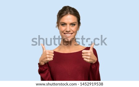 Blonde woman with thumbs up because something good has happened over isolated blue background