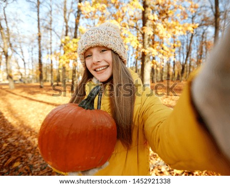 season and people concept - happy girl with pumpkin taking selfie at autumn park