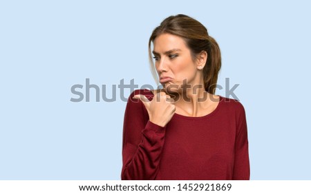 Blonde woman unhappy and pointing to the side over isolated blue background