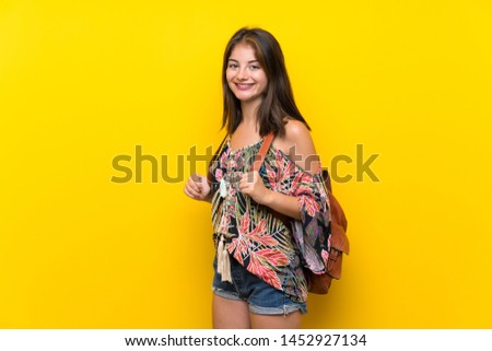 Caucasian girl in colorful dress over isolated yellow background with backpack