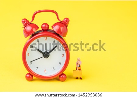 Travel time, reminder for airline checkin for traveller concept, miniature people young lady with luggages or baggage standing with red alarm clock on solid yellow background with copy space.